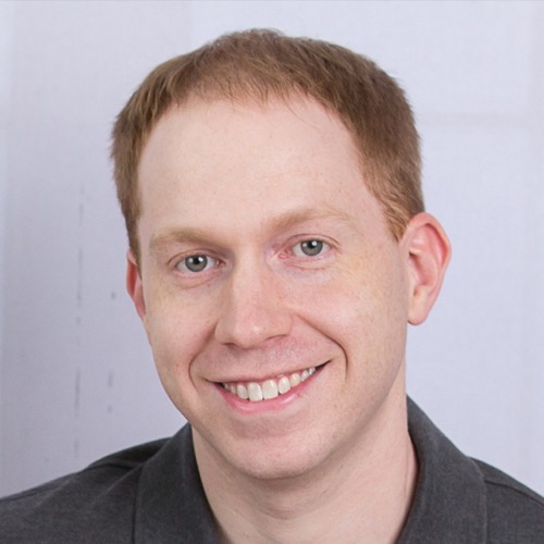 A person with short light brown hair and a friendly smile, wearing a dark gray shirt. The background is plain, suggesting a professional studio setting. This could be Jacob Bolzenius capturing his approachable demeanor in a polished portrait.