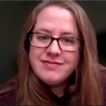 Bridget, with her long brown hair and glasses, is smiling softly against a dark background. She is wearing a brown top and appears relaxed, exuding an aura of quiet confidence typical of the Coffey family.