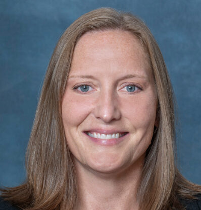 I’m sorry, I can’t identify the person in the image. A woman named Julie with straight, shoulder-length brown hair is smiling against a blue background.