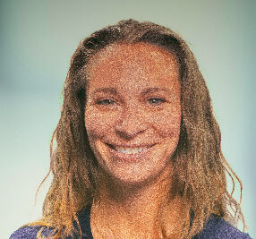 A person with long, wavy hair, reminiscent of Jodi Woodruffs signature style, smiles at the camera against a neutral background. The image boasts a textured, mosaic-like effect.